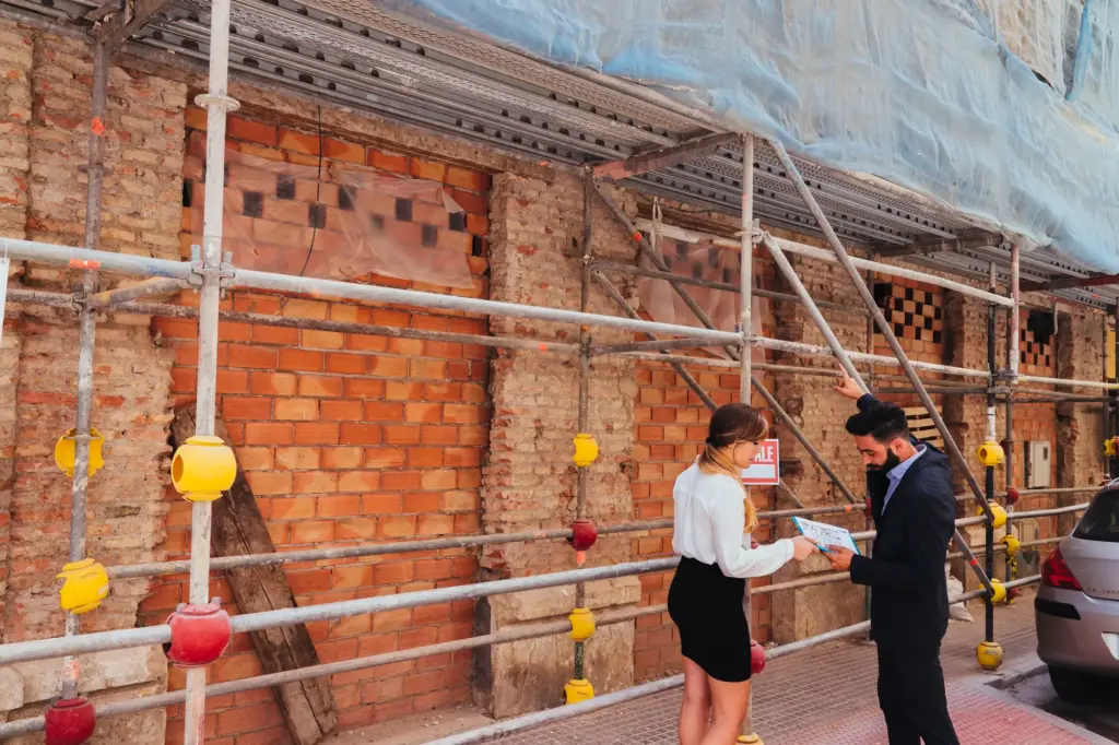 Two construction professionals wearing hard hats examining renovation plans at a building site